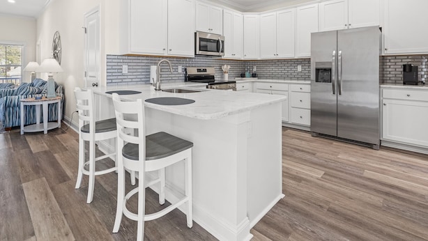 A modern kitchen with white cabinetry, a central island with bar stools, stainless steel appliances, and a brick backsplash. - Private Luxury 4BR North Myrtle Beach Home with Saltwater Pool & Fenced Backyard (North Myrtle Beach)