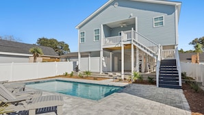 A two-story house with a pool, a covered patio, and a staircase leading to the upper level. - Private Luxury 4BR North Myrtle Beach Home with Saltwater Pool & Fenced Backyard (North Myrtle Beach)