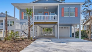 A two-story house with a balcony, a garage, and a covered walkway. - Private Luxury 4BR North Myrtle Beach Home with Saltwater Pool & Fenced Backyard (North Myrtle Beach)