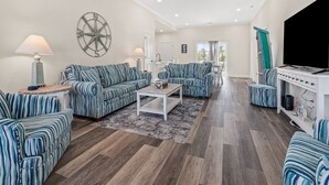 A spacious living room with striped sofas, a coffee table, and a TV stand. - Private Luxury 4BR North Myrtle Beach Home with Saltwater Pool & Fenced Backyard (North Myrtle Beach)