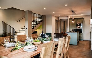 A dining area with a wooden table set for four, a staircase with a railing, and a kitchen in the background. - Awesome home in Bribir (Bribir)