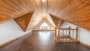 A spacious attic room with wooden slats on the ceiling, a large window, and a wooden bed frame. - Geoje Blueberry Pet Pension (Geoje)
