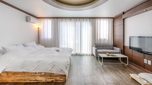 A modern hotel room with a large bed, a grey armchair, a small table with a cup and flowers, a flat-screen TV, and a wooden floor. - Geoje Blueberry Pet Pension (Geoje)