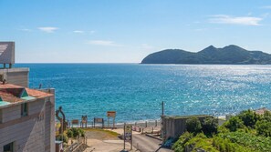 Blick auf die Küste mit blauem Meer, einem Berg in der Ferne und einer Straße, die zu einem Gebäude mit Beschilderung führt.