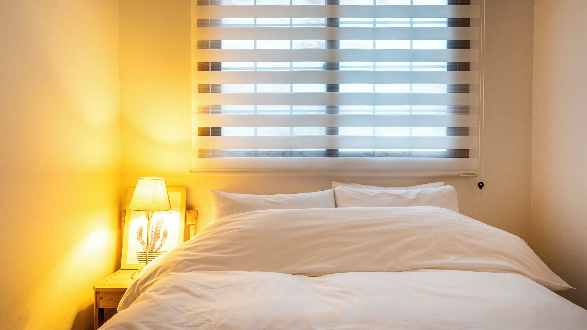 A bedroom with a bed, a nightstand, a lamp, and a window with blinds.