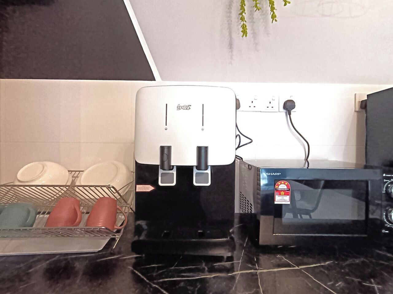 Una cocina con cafetera, microondas y escurreplatos con vajilla.