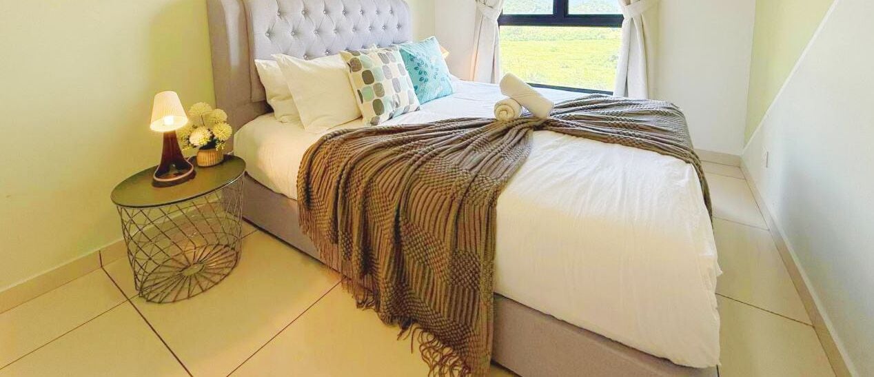 Een slaapkamer met een queensize bed, een nachtkastje met lamp, en uitzicht op de omgeving door een raam.