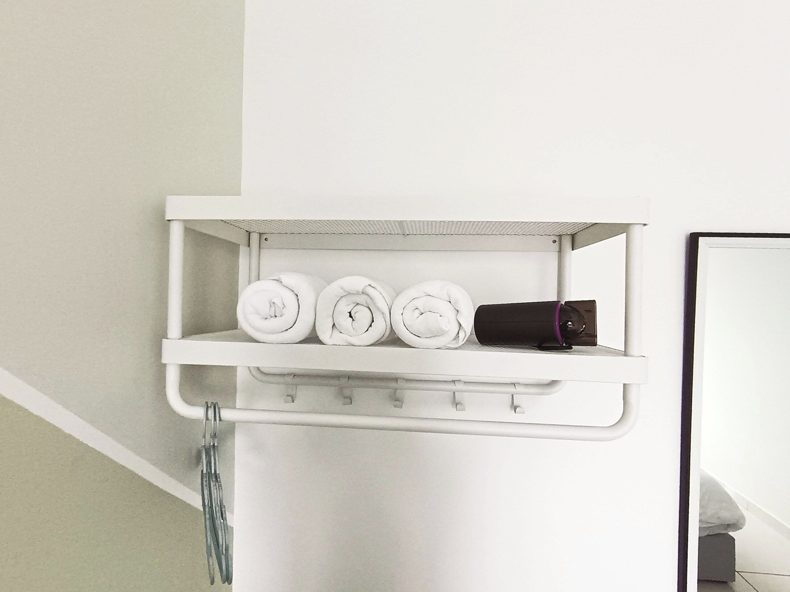 A white shelf with rolled towels and a black object, likely a hairdryer, in a bathroom setting.