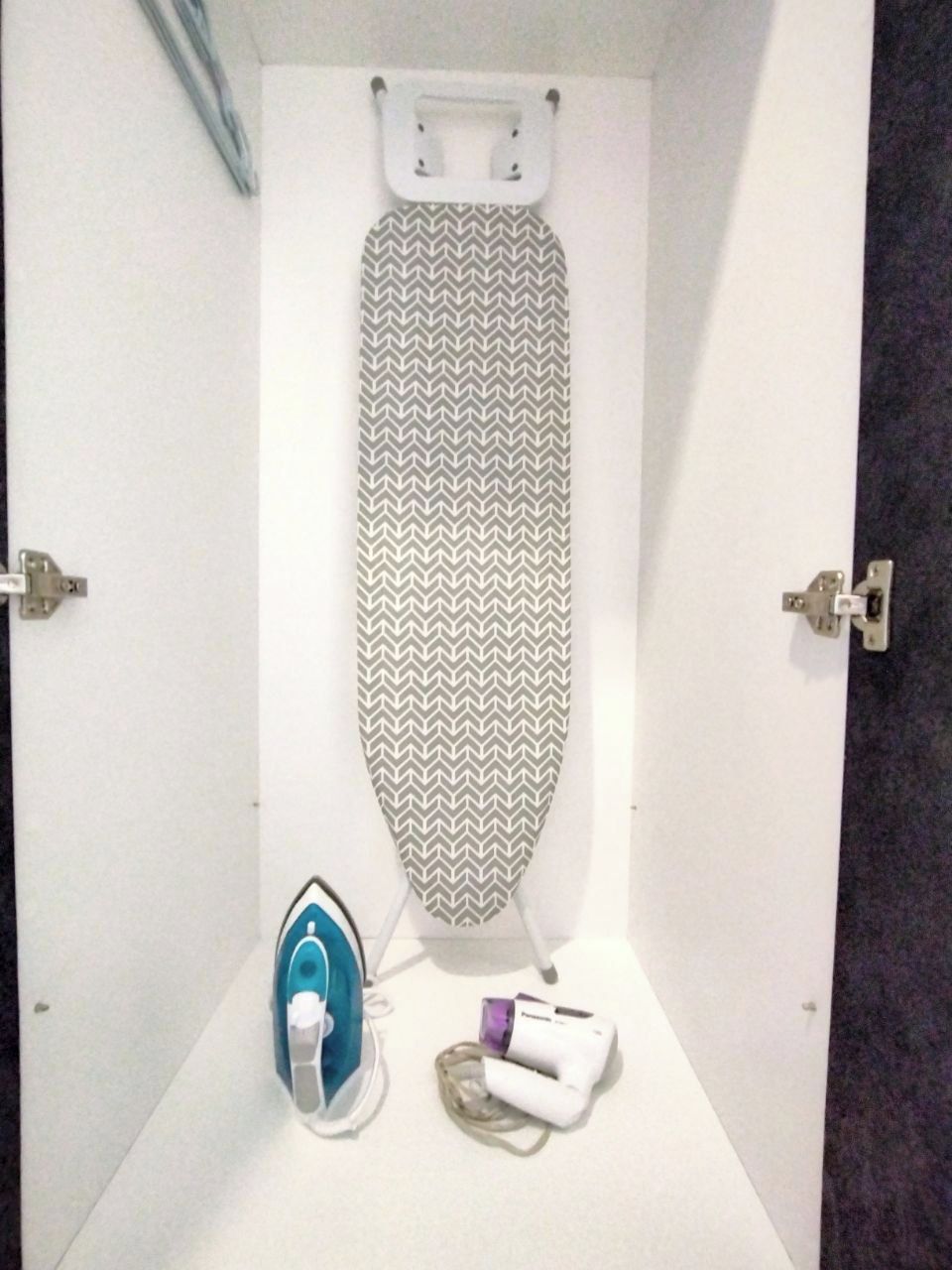 A small, enclosed space with an ironing board, an iron, and a hairdryer.