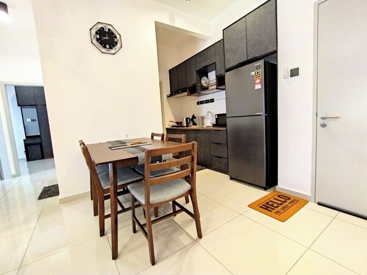 A modern kitchen with dark cabinets, a stainless steel refrigerator, and a dining area with wooden chairs and a table.