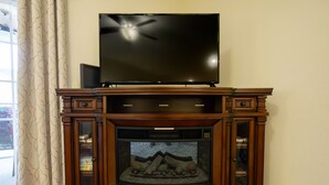Un meuble de rangement en bois, avec un téléviseur à écran plat posé sur le dessus, une cheminée avec une porte en verre et un rideau à motifs sur le côté gauche.