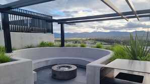 Un espace extérieur moderne, aménagé pour se détendre, avec un design en béton aux lignes courbes, un foyer intégré et une vue sur les montagnes lointaines.