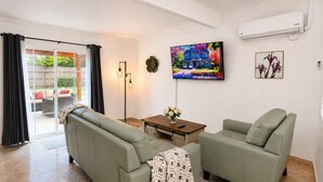 Een woonkamer met een bank, fauteuil, salontafel en een aan de muur bevestigde televisie.