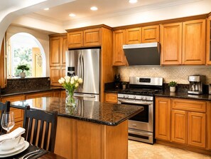 A modern kitchen with wooden cabinets, stainless steel appliances, and a central island. - Midterm Rental: Peaceful House with Big Yard, AC, Wifi, Laundry, Tesla Charger.. (Pico Rivera)