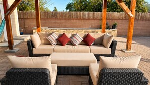 Een terras met een bank en twee fauteuils, een houten pergola en een bakstenen muur op de achtergrond.