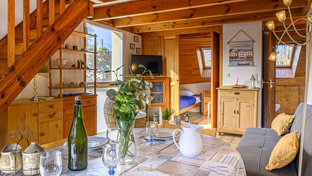 Een gezellig chaletinterieur met een eethoek, een bank en een slaapkamer met dakraam.