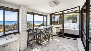 Ein Balkon mit Meerblick, ein Essbereich mit Stühlen und Tisch sowie eine Couch mit Kissen.