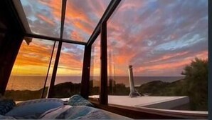 Ein Zimmer mit einem großen Fenster, das einen Blick auf einen Sonnenuntergang über einer Küstenlandschaft bietet.