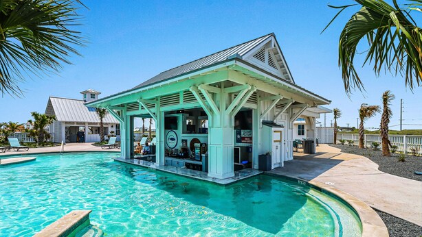 Zona de piscina con bar, palmeras y una piscina azul cristalina.