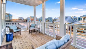 Un espacio al aire libre techado con muebles de mimbre, piso de madera y vistas a casas al fondo.