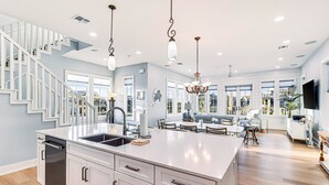 Una cocina amplia con una isla central, armarios blancos y una lámpara moderna.