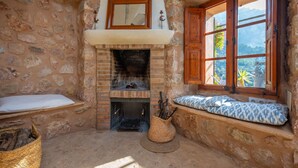 A rustic stone-walled room with a fireplace, a window with wooden shutters, and a bench with a patterned cushion. - SA TEULERA (FORNALUTX) - Fabulous house with stunning views of the Serra de Tramuntana - F (Fornalutx)