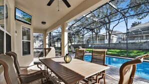 A covered patio with a pool, outdoor furniture, and a television screen displaying a beach scene. - Windsor Hills Resort 6 Bedroom Private Pool+Spa Home (Kissimmee)