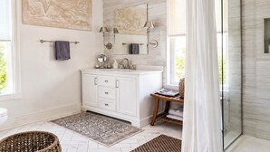 A modern bathroom with a white vanity, a glass shower enclosure, and artwork on the walls.
