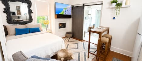 Un dormitorio moderno con una cama grande, televisor, chimenea y una mesita.