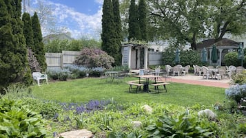 A well-maintained garden with a patio area featuring tables and chairs, surrounded by various plants and trees.