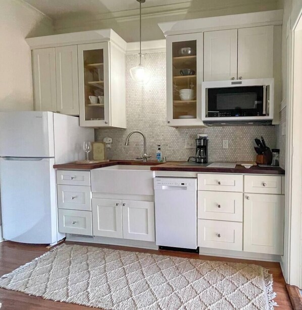 Una cucina con mobili bianchi, un forno a microonde, una lavastoviglie e un lavello.