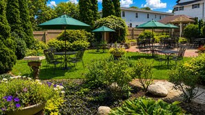 A well-maintained outdoor patio area with multiple tables and chairs, surrounded by lush greenery and flowering plants. - Historic Downtown Luxury-Lake-Coffee-Spa like BA (Delafield)