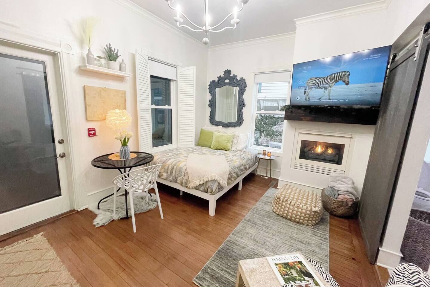 A cozy bedroom with a bed, a small table, a chair, a fireplace, and a TV displaying a zebra.