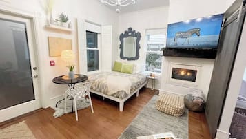 A cozy bedroom with a bed, a small table, a chair, a fireplace, and a TV displaying a zebra.