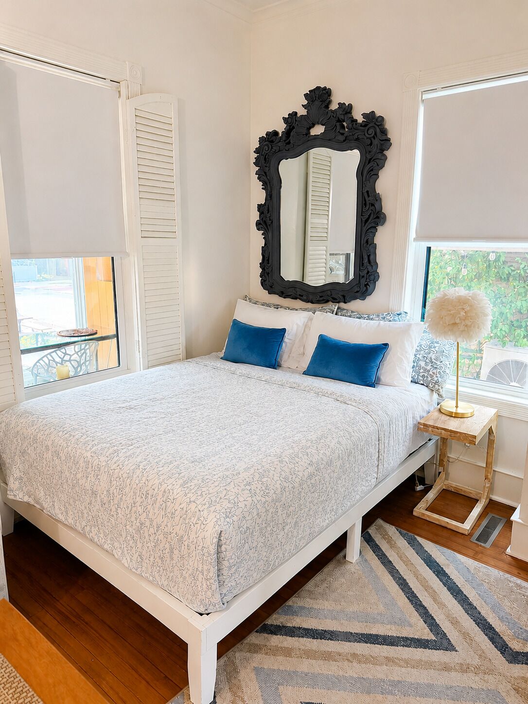 A bedroom with a bed, a mirror, a window, and a bedside table.