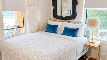 A bedroom with a bed, a mirror, a window, and a bedside table.