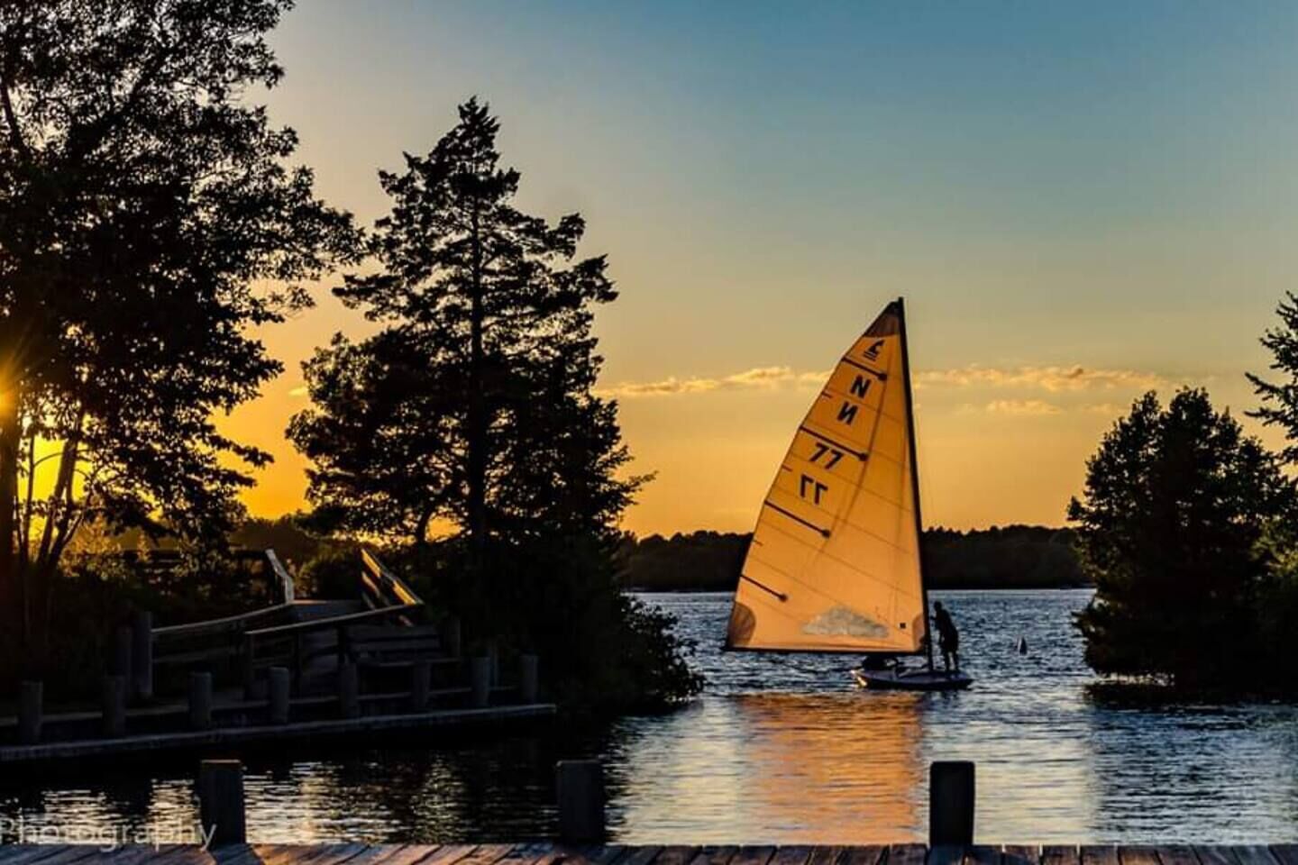 A sailboat with a sail marked with numbers on a body of water at sunset.