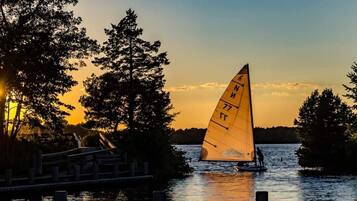 A sailboat with a sail marked with numbers on a body of water at sunset.