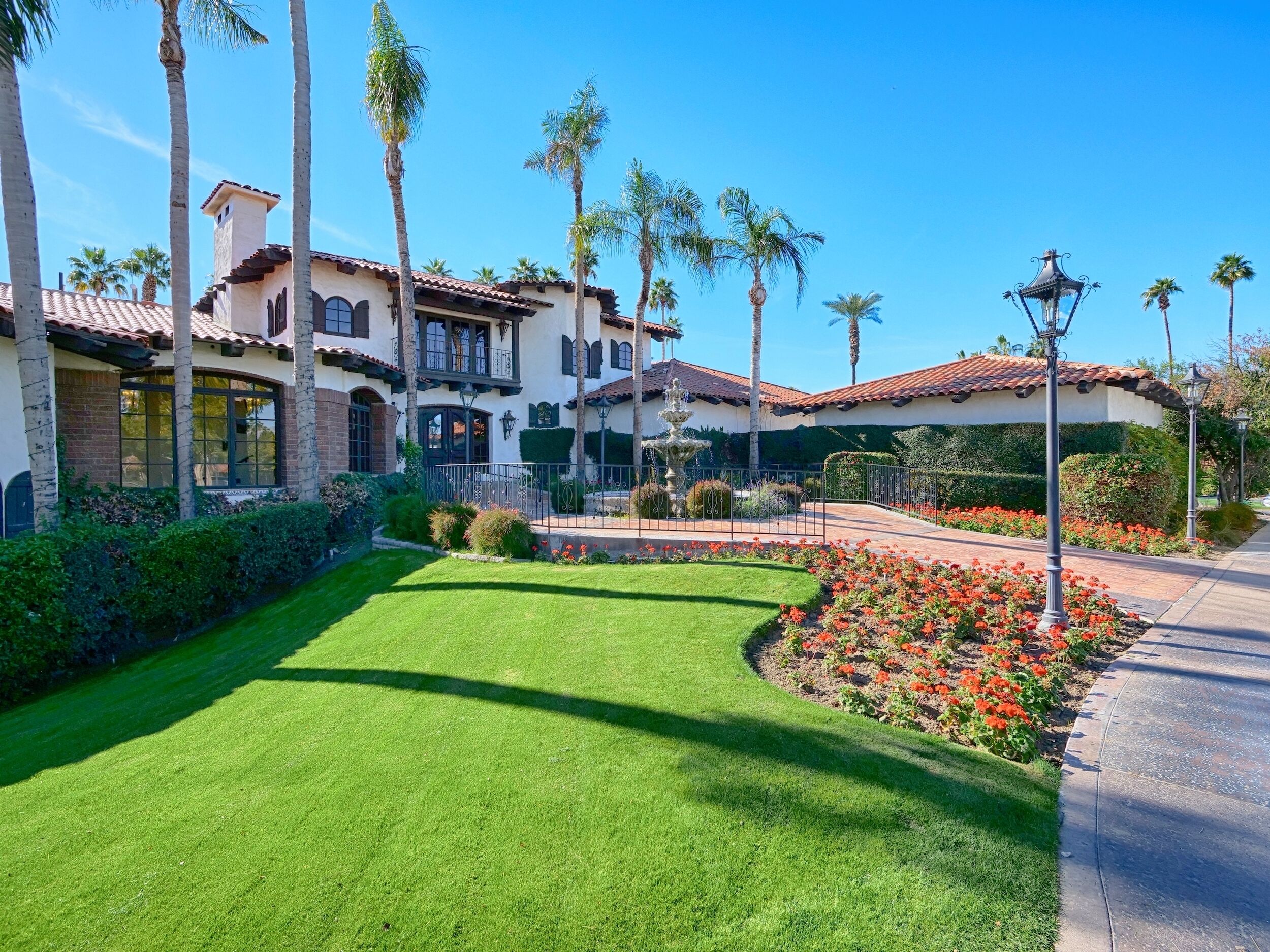 A Mediterranean-style villa with a well-manicured lawn, palm trees, and a fountain.