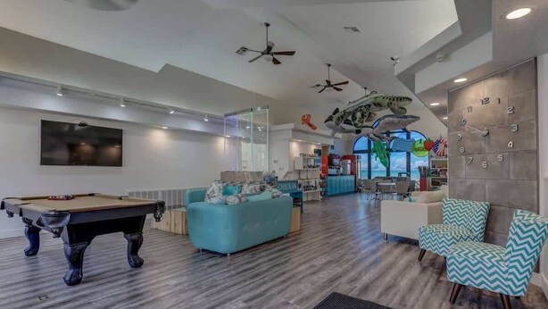 A spacious indoor area with a pool table, seating, ceiling fans, and a large clock on the wall. - Las Palmas 1644 Pools Waterpark Resort (St. George)