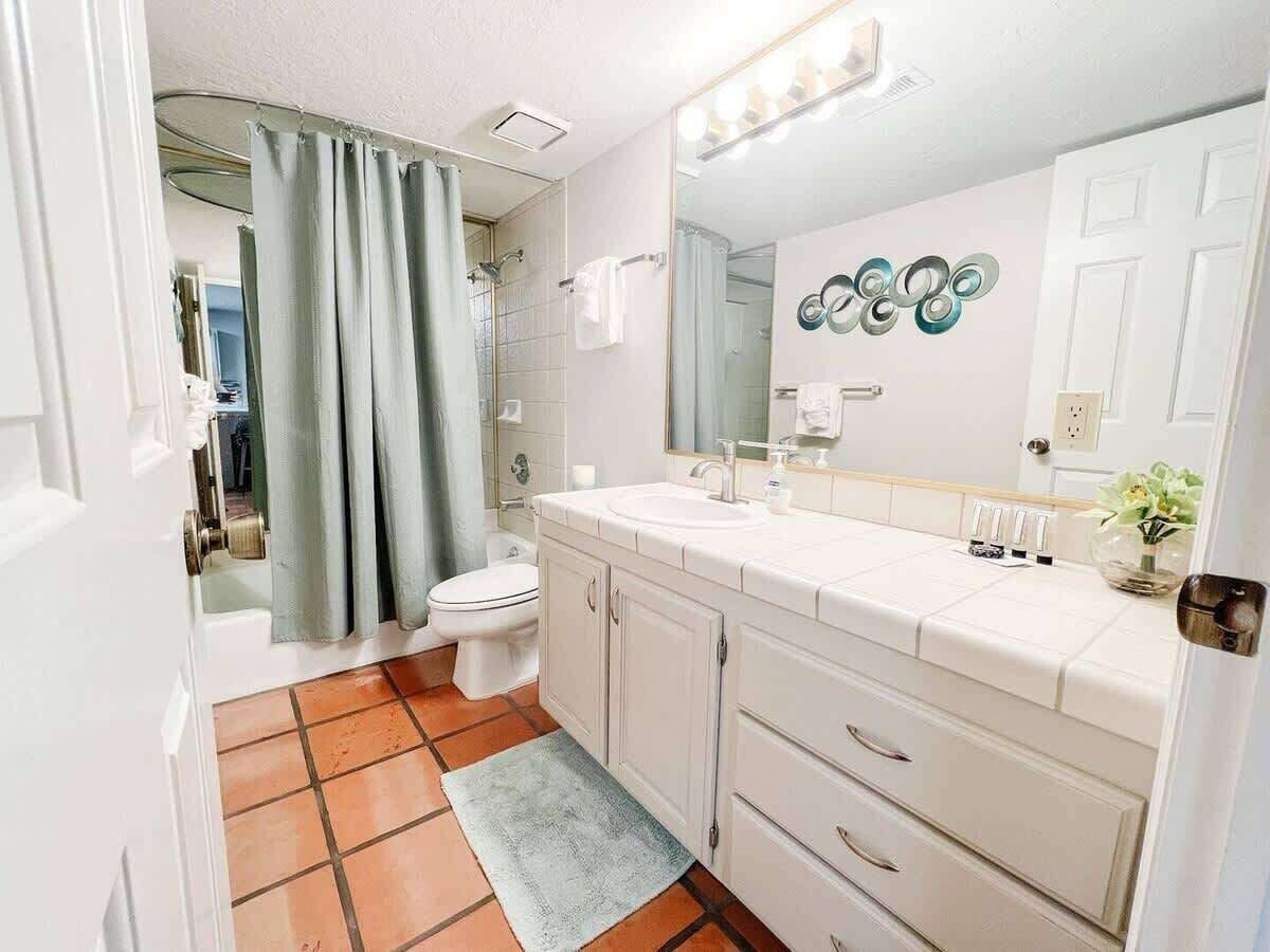 A bathroom with a white sink, mirror, and cabinet, a shower curtain, and a toilet.