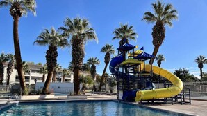 A swimming pool with a water slide, surrounded by palm trees and a clear blue sky. - Las Palmas 1644 Pools Waterpark Resort (St. George)