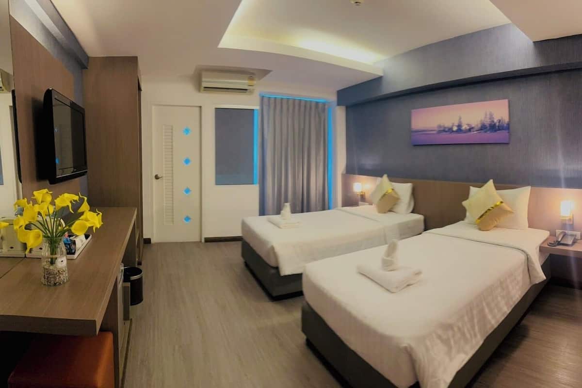 A hotel room with two beds, a TV, a desk with a vase of flowers, and a painting on the wall.