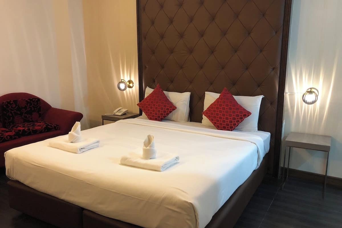 A hotel room with a large bed, a red armchair, a nightstand with a phone, and two wall sconces.