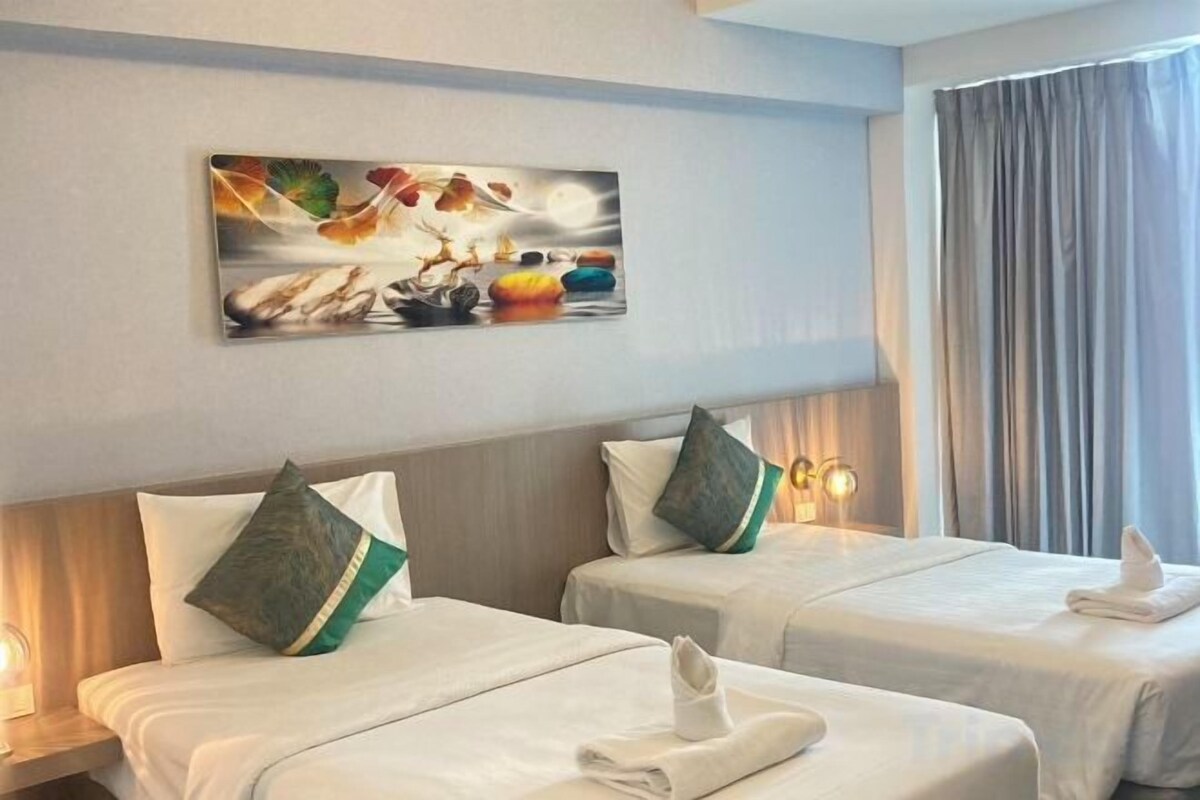 Hotellihuone, jossa on kaksi sänkyä, seinällä taulu ja ikkunassa verhot.
