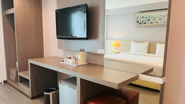 Een moderne hotelkamer met een flatscreen televisie, een bureau met koffiezetapparaat en een bed met nachtkastje.