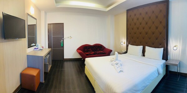 A hotel room with a bed, a desk, a chair, a TV, and a door. - Kann Pattaya Hotel (Pattaya)