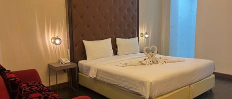 A hotel room with a large bed, a red armchair, a bedside table with a phone, and a wall-mounted air conditioner.