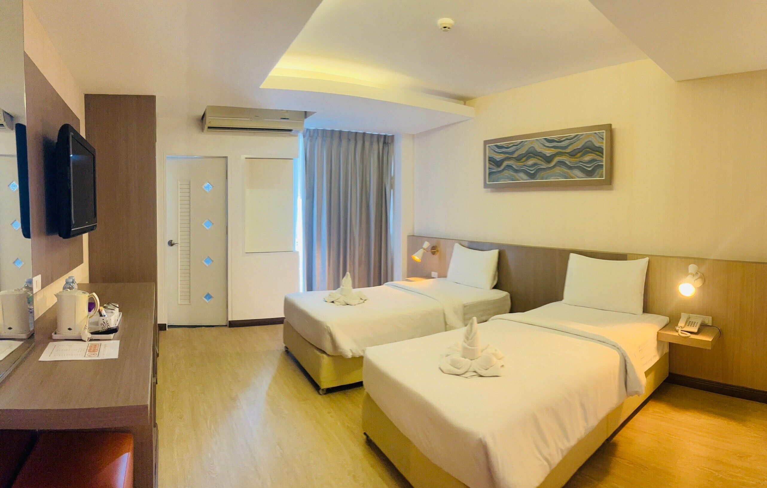 A hotel room with two beds, a desk with a telephone, and a television.
