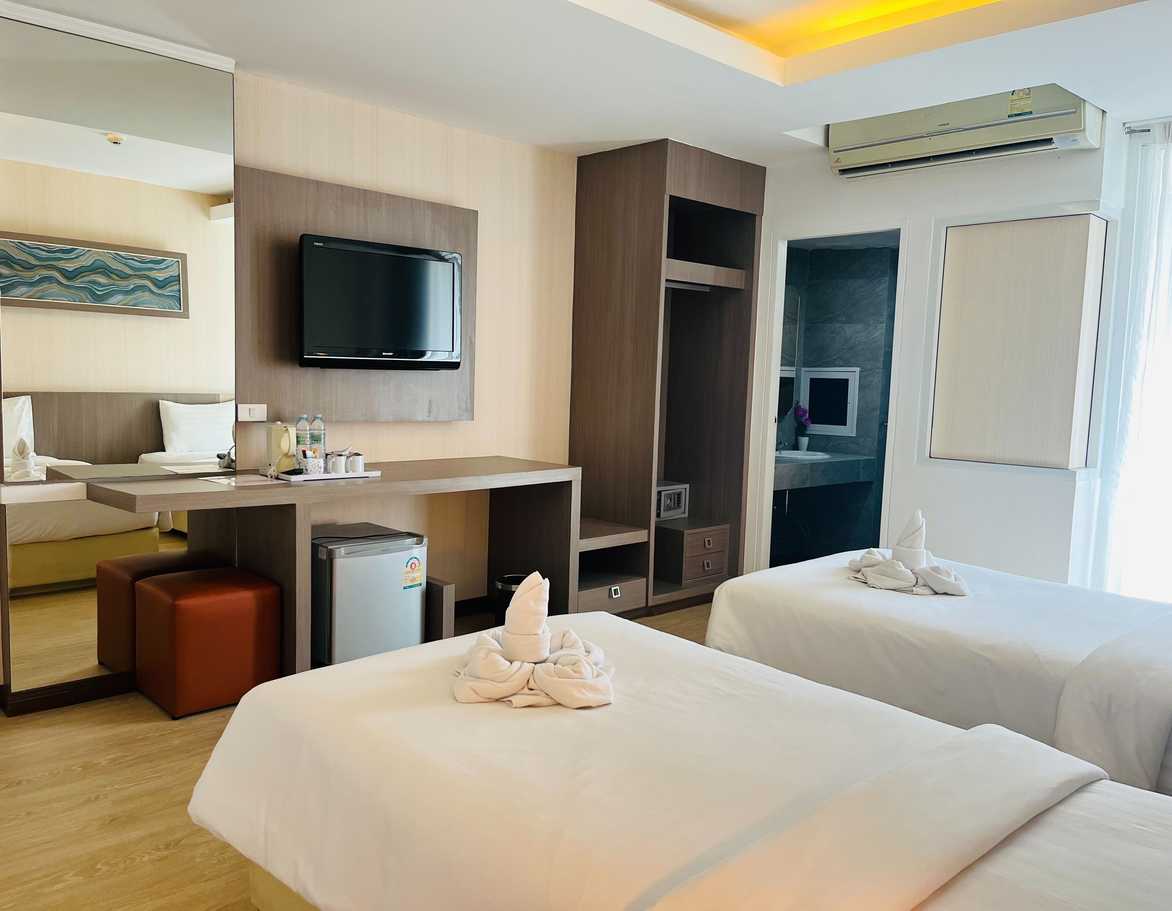 A hotel room with two beds, a desk, a television, a minibar, and a bathroom visible through an open door.